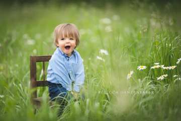 Baby boy sitting outside on a wooden chair in a flower field