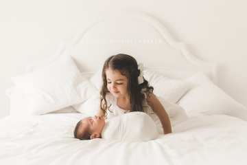 Newborn baby and her older sister in white studio bedroom Newborn baby and her older sister in white studio bedroom